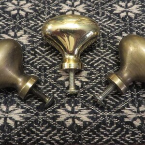 May include: Three oval-shaped metal cabinet knobs with a polished brass finish. Each knob features a smooth, rounded head and a threaded metal screw extending from the base for attachment to furniture or cabinetry doors and drawers.