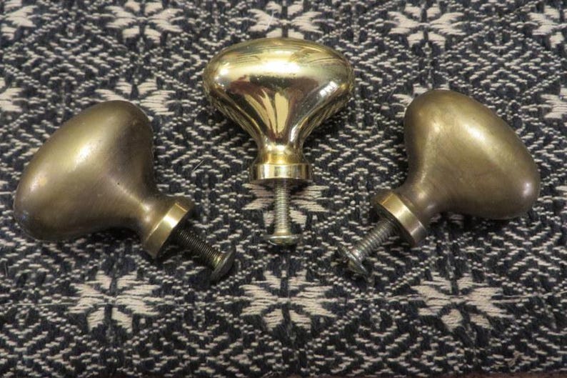 May include: Three oval-shaped metal cabinet knobs with a polished brass finish. Each knob features a smooth, rounded head and a threaded metal screw extending from the base for attachment to furniture or cabinetry doors and drawers.