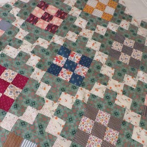 May include: A patchwork quilt with a repeating pattern of squares and diamonds. The quilt features a variety of fabrics in shades of green, white, pink, red, blue, and brown. The design is a mix of floral and geometric patterns.