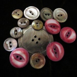 May include: A selection of buttons in various sizes and colours. The buttons include iridescent mother-of-pearl, brown, and red with white accents. The buttons have two or four holes for sewing and are arranged on a black surface.