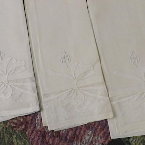 May include: Three rectangular off-white linen guest towels featuring an embroidered bow design at the bottom. Each towel includes a sheer panel with a subtle dotted pattern and a delicate monogram stitched in white thread above the bow motif.