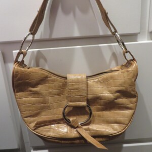 May include: A tan leather handbag with a crocodile embossed pattern and a silver ring detail. The bag has a single strap and a flap closure.
