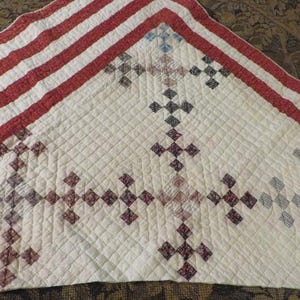 May include: A handmade quilt with a white background and a pattern of red and dark red cross-like shapes. The border features red and white stripes. The quilt is likely made of cotton and has a diamond-stitched pattern.