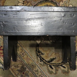 May include: A black wooden stool with a simple design. The stool has a rectangular top and two legs on each side. The stool is made of wood and has a black finish.