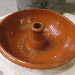 Puede incluir: Un molde para hornear de cerámica de color terracota con un molde central en forma de cono. El molde está diseñado para hornear pasteles bundt u otros postres con forma de anillo.
