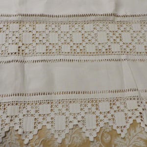 May include: White crocheted lace trim with a scalloped edge. The lace has a repeating pattern of squares and is made with delicate stitches.