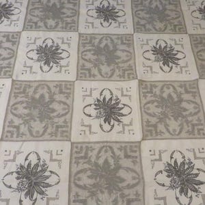 May include: A textile fabric featuring a repeating grid pattern of alternating light beige and muted gray squares. Each square displays a central floral motif surrounded by geometric corner accents, creating a consistent, symmetrical design.