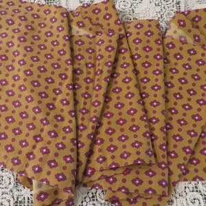 May include: A stack of fabric squares with a repeating pattern of small burgundy and white diamonds on a mustard yellow background.