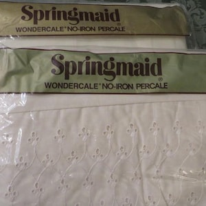 May include: Two packages of off-white Springmaid Wondercale no-iron percale fabric. The packaging features the brand name in dark brown text on a gold band. The fabric inside is visible, showing a white eyelet embroidery pattern with floral motifs.