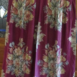 May include: Burgundy fabric with a floral pattern featuring roses, tulips, and other flowers in shades of yellow, peach, and white. The fabric is pleated and appears to be a curtain or drapery.