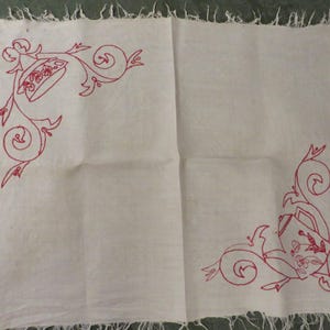 May include: White linen tablecloth with red embroidered floral designs in the corners. The tablecloth has a frayed edge.