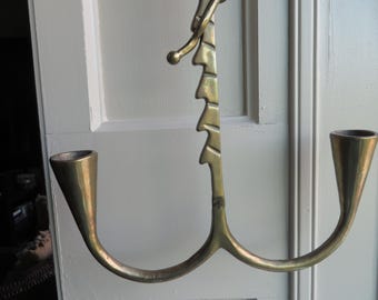 May include: A vintage brass candle holder with a unique, abstract design. The holder features two curved arms with conical candle cups and a central decorative element with a series of stylized shapes. The brass has a warm, aged patina.