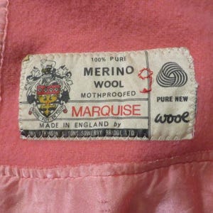 May include: A rectangular fabric label sewn onto a pink wool garment. The label features a crest, the text 100% PURE MERINO WOOL MOTHPROOFED MARQUISE MADE IN ENGLAND BY J.N. ATKINSON & SONS SOWERBY BRIDGE LTD, and a PURE NEW WOOL yarn ball icon.