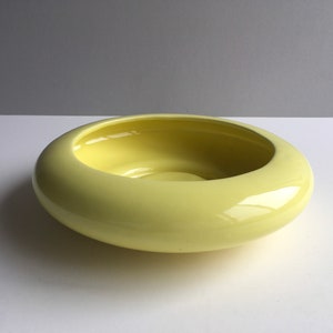 May include: A pale yellow ceramic bowl with a rounded, slightly flared rim. The bowl has a smooth, glossy finish.