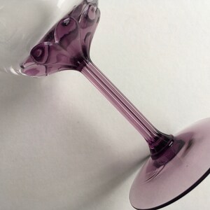 May include: A purple glass wine glass with a decorative swirl design on the stem and base.
