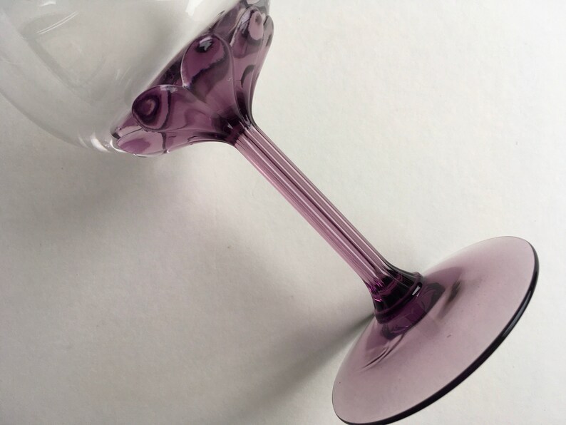 May include: A purple glass wine glass with a decorative swirl design on the stem and base.