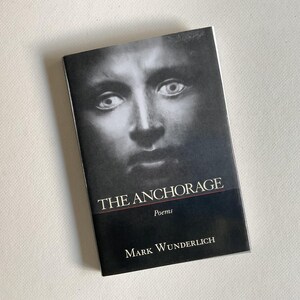 May include: A paperback book titled "THE ANCHORAGE" with a black and white portrait on the cover. The cover features a grayscale image of a person's face. The author's name, Mark Wunderlich, is printed at the bottom.