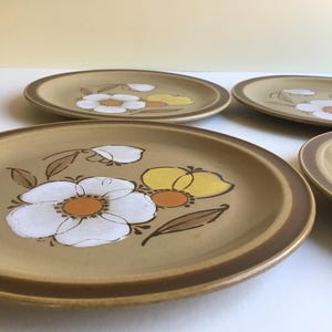 May include: Set of four brown stoneware dinner plates with a floral design featuring white, yellow, and orange flowers.