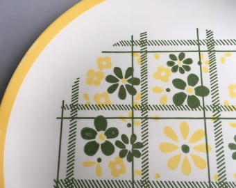 May include: A white ceramic plate with a yellow rim and a green and yellow floral pattern. The pattern features a plaid design with small flowers.