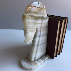 May include: A pair of bookends made of white and brown onyx, shaped like a horse's head. The bookends are holding up a stack of books with brown covers.