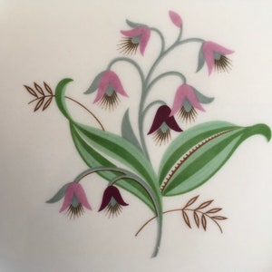 May include: A white ceramic plate with a floral design featuring pink and purple flowers with green leaves and brown stems.