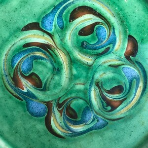 May include: A green ceramic plate with a swirling pattern of brown, blue, and gold paint.