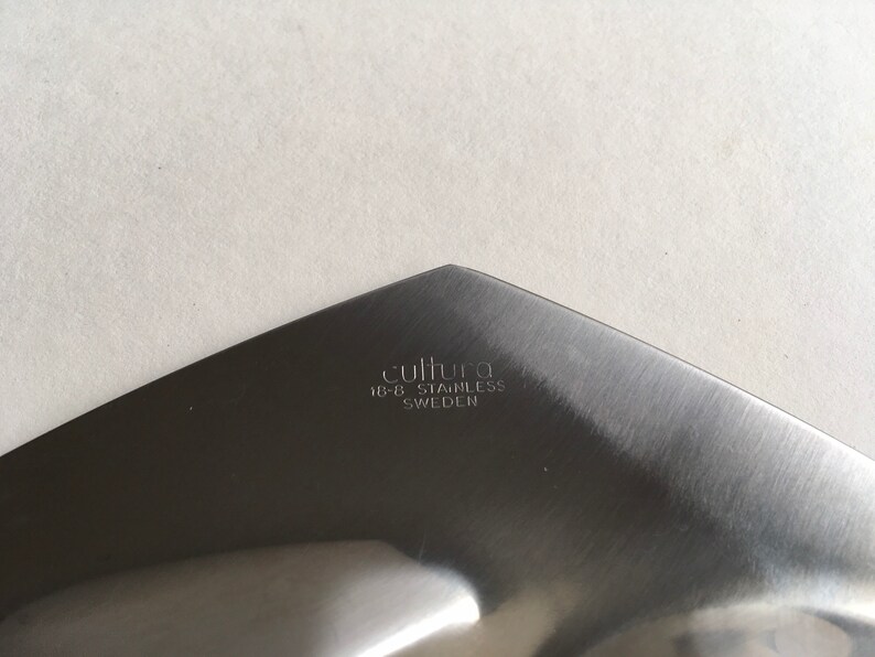 Pu&ograve; includere: Primo piano del fondo di un utensile da portata argentato con il testo "cultura 18-8 stainless SWEDEN" inciso sulla superficie.