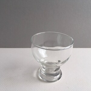 May include: A clear glass bowl with a wide base and a rounded top. The bowl is empty and sits on a white surface.