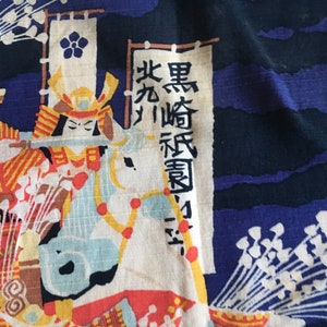 May include: A blue and white fabric featuring a Japanese warrior riding a horse. The warrior is wearing a helmet and armour. The fabric has a white flower design and the text "黒崎 辰 勇" in Japanese.