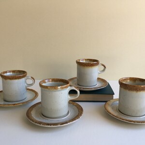 May include: Set of four brown and white ceramic coffee cups and saucers. The cups and saucers have a speckled glaze.