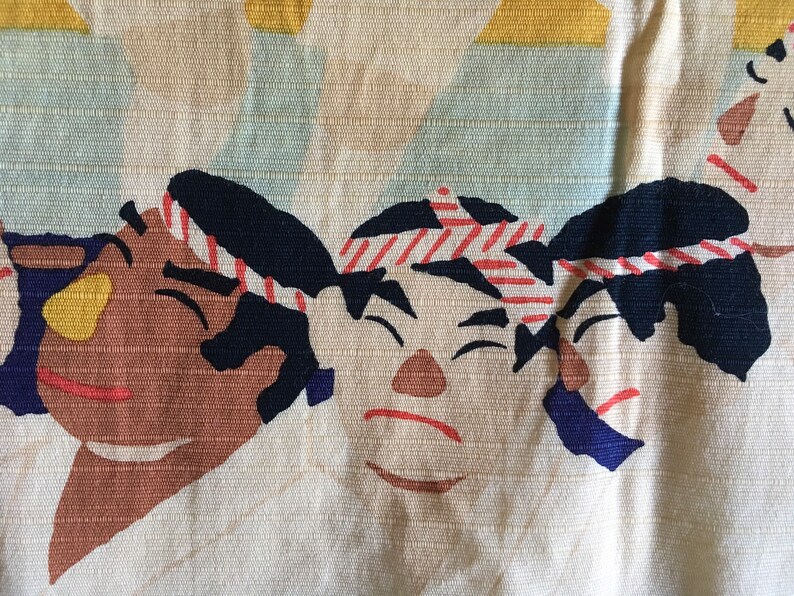 May include: Three cartoon faces with black hair and red and white striped headbands. The faces are brown, tan, and white with black eyes and red mouths. The background is a light beige fabric.