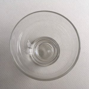 May include: A clear glass bowl with a smaller, concentric bowl inside. The bowl is empty and appears to be made of thick glass.