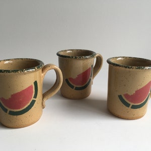 May include: Three ceramic mugs with a speckled beige glaze and a green and red watermelon design.