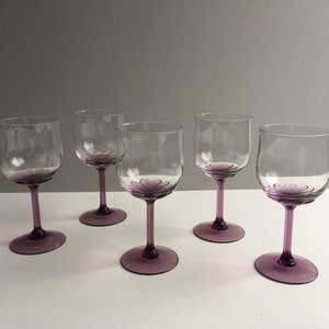 May include: Set of four clear glass wine glasses with purple tinted stems and bases. The glasses have a rounded bowl shape.