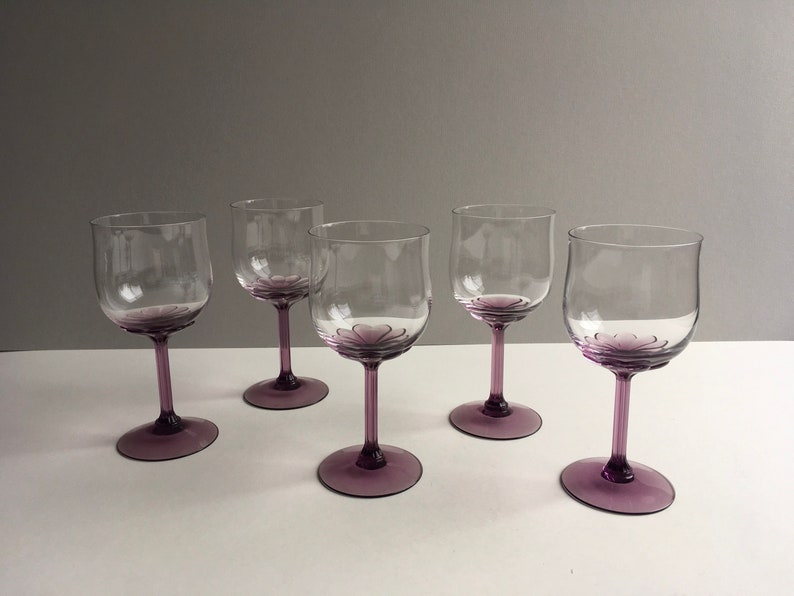 May include: Set of four clear glass wine glasses with purple tinted stems and bases. The glasses have a rounded bowl shape.