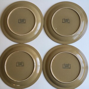 May include: Four brown ceramic dinner plates with a raised rim and a brown and white logo that reads "Earthenware Made in Japan" in the center.