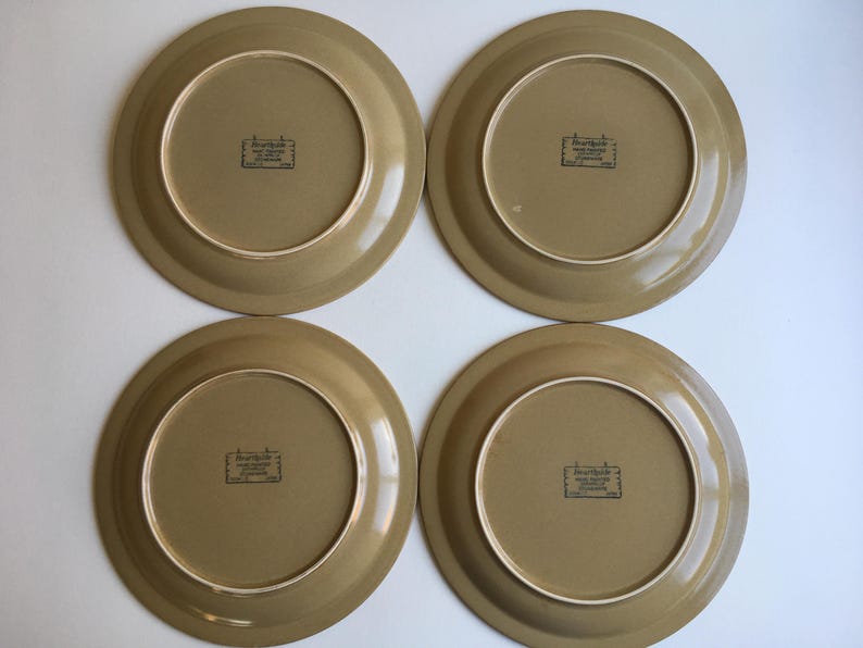May include: Four brown ceramic dinner plates with a raised rim and a brown and white logo that reads "Earthenware Made in Japan" in the center.
