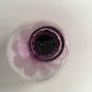 May include: Close-up of the base of a purple glass bowl with a "Fostoria" logo.