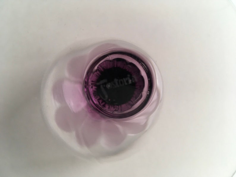 May include: Close-up of the base of a purple glass bowl with a "Fostoria" logo.