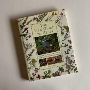 May include: A book titled "The New Guide to Herbs" with a green, blue, and white color scheme. The cover features a variety of dried herbs and flowers, including lavender, rosemary, and thyme. The book also includes a section on the cultivation and uses of herbs.