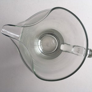 May include: A clear glass pitcher with a wide mouth and a handle. The pitcher has a textured, ribbed design.