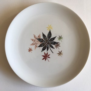 May include: White ceramic dinner plate with a stylized design of brown, black, and green leaves.
