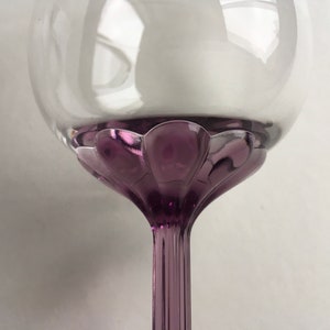 Op de afbeelding: Een helder glazen wijnglas met een paarse steel en voet. De voet heeft een gegolfd ontwerp.
