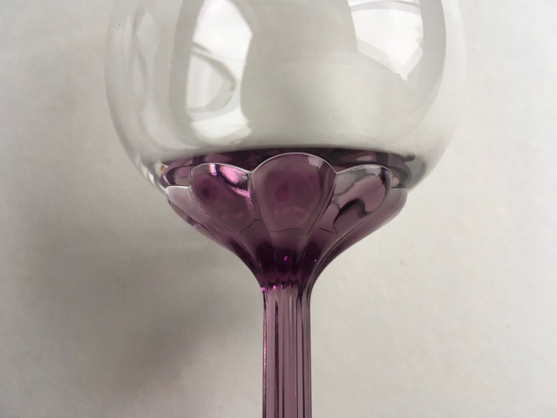 Op de afbeelding: Een helder glazen wijnglas met een paarse steel en voet. De voet heeft een gegolfd ontwerp.