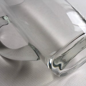 May include: A clear glass mug with a handle. The mug is empty and has a rounded bottom.