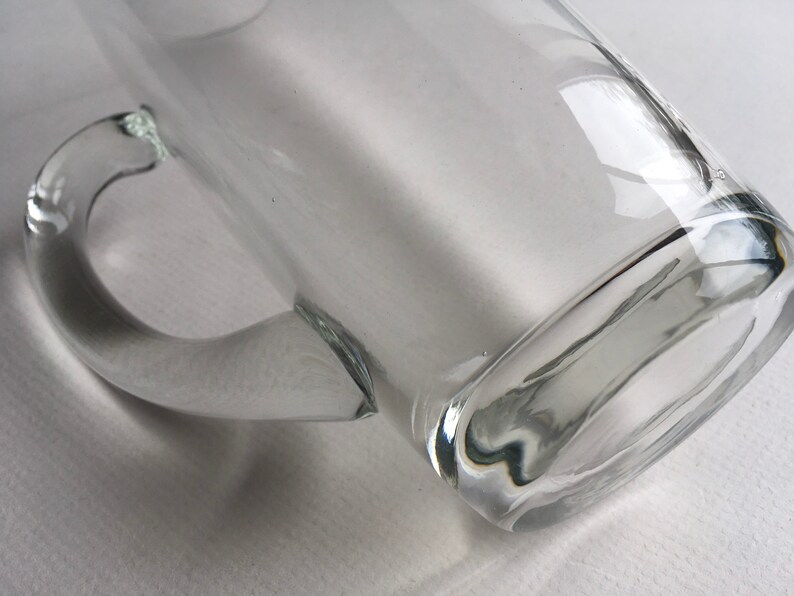 May include: A clear glass mug with a handle. The mug is empty and has a rounded bottom.
