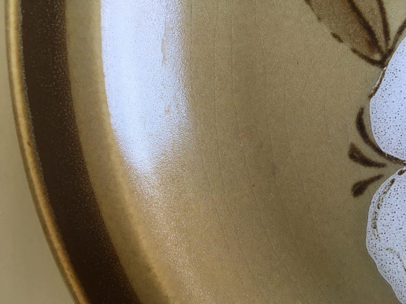 May include: A brown ceramic plate with a white floral design. The plate has a brown rim and a textured surface.
