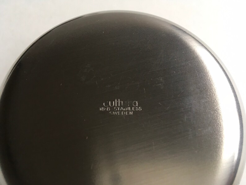 Pu&ograve; includere: Il fondo di una ciotola di metallo argentata con il testo "cultura 18-8 stainless SWEDEN" inciso sulla superficie.