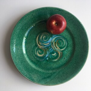 May include: A green ceramic plate with a swirl design and a red apple on top.