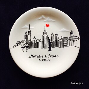 May include: White ceramic plate featuring a black and white illustration of the Las Vegas skyline, including the Bellagio, the Wynn, and the Luxor. The plate also has a red heart above the skyline and the text "Natalie & Brian 1.20.17".